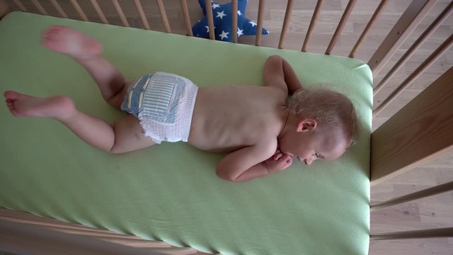 Active baby boy child in diapers lying in a wooden bed. Gimbal movement
