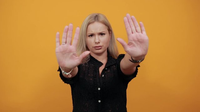 Beautiful blonde girl in black dress on yellow background irritated angry woman stops with her hands shows palms