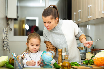 Mother cooking and little daughter  doing school homework