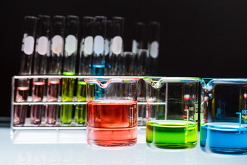 red, green and blue chemical liquid sample containing in beakers with lab glassware on black...