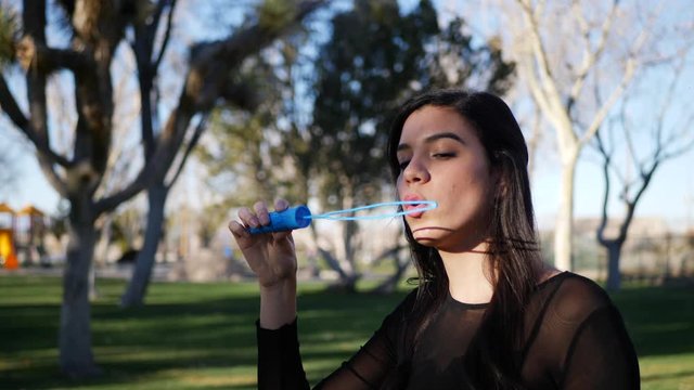 A cute young woman blowing bubbles and frowning in comical failure as they pop in a funny way.