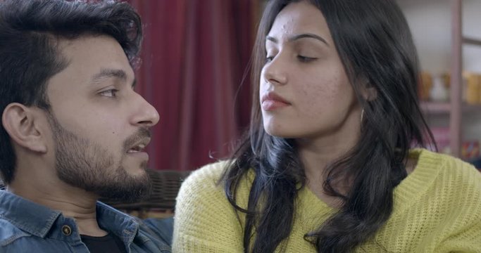 Couple intimate having an argument . discussion conflict over a smart phone mobile phone indoors seated in living room, woman is pissed and guy apologies and says sorry. 60fps slow-motion  handheld