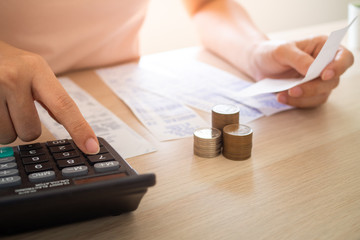 The woman sitting and examining the bill press the calculator to calculate the amount of income, expenses and expenses on the table. Inside the living room at home.