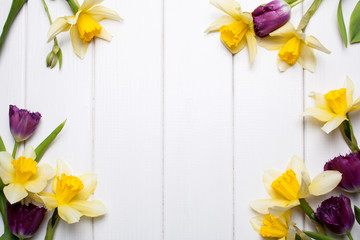 Spring frame with yellow flowers daffodil and tulips on a white wooden background in flat lay style