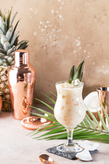 Pina Colada Cocktail on sand beige background with tropical fruits and bar tools, summer relaxation...