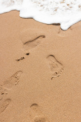 Footprints on the sand of the beach and white color of sea wave bubble