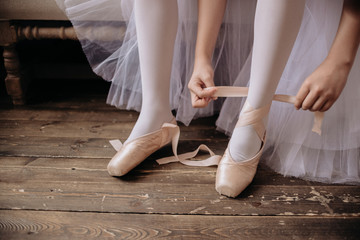 Ballet dancer's feet on studio floor. Teenage dancer puts on ballet pointe shoes. Elegance and balance concept top horizontal view copyspace.