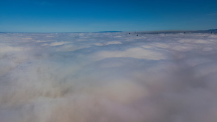 Landscape over the clouds in foggy weather. Hills of buildings in foggy weather. The drone and the top of the fog layer.