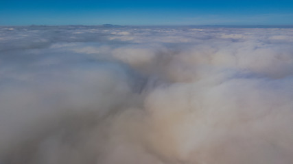 Landscape over the clouds in foggy weather. Hills of buildings in foggy weather. The drone and the top of the fog layer.