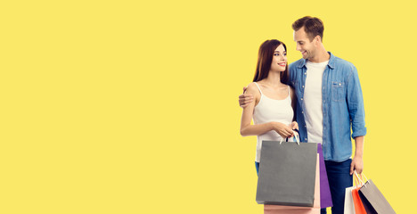 Love, holiday sales, shop, retail, consumer concept - happy couple with shopping bags, looking at each other. Yellow color background. Copy space for some text.