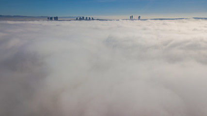 Landscape over the clouds in foggy weather. Hills of buildings in foggy weather. The drone and the top of the fog layer.