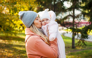 Fototapeta premium Young beautiful woman hugs and kisses her little daughter in park. Love mom and baby.
