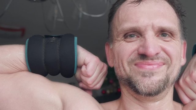 Mature man smiles and shows off his bicep with weighter. BCU