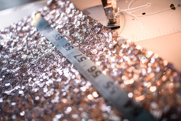 Close-up photo of sewing machine with shiny piece of fabric and measuring tape.