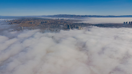 Landscape over the clouds in foggy weather. Hills of buildings in foggy weather. The drone and the top of the fog layer.