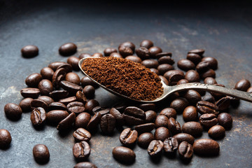 Ground coffee in a spoon and beans on a grunge dark background