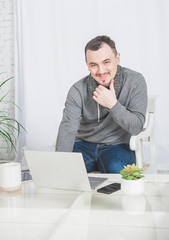 Fototapeta premium Handsome happy man working using laptop with smartphone at home