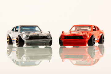 Two toy muscle car on white with reflection
