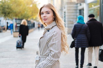 Beautiful casual blond girl thoughtfully looking in camera on street