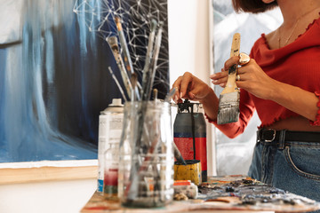 Portrait of young woman using painting tools while drawing in studio