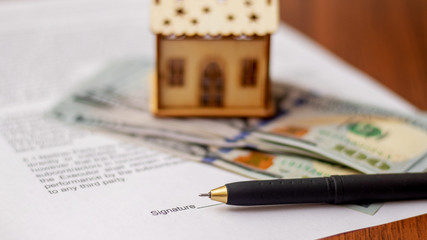 Handle for signing a document on the sale and purchase of a house. Model of the house near the money and the document on the purchase of housing_