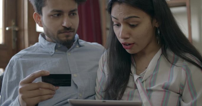 Indian couple with a touch screen tablet with credit card make a financial and economic plan to make their savings in development economy as they both work overtime, handheld slow-motion 60fps