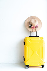 A hat hang on a yellow luggage in front of white wall.