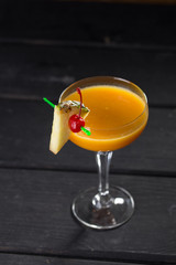 yellow alcohol cocktail with pineapple and cherry in martini glass on black wooden table