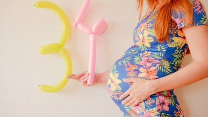 A close up photo of a pregnant young woman holding in her hands the week number thirty four (34) next to her belly in a beautiful dress. Photos of a pregnant woman in the third trimester expecting.