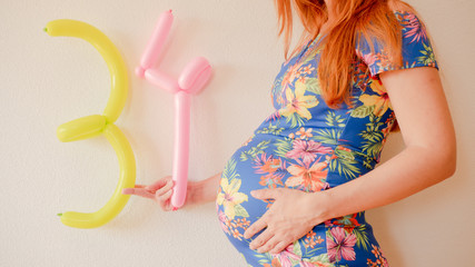 A close up photo of a pregnant young woman holding in her hands the week number thirty four (34)...