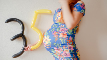 A close up photo of a pregnant young woman holding in her hands the week number thirty five (35)...