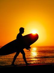 male surfer walking with his table in a sunset