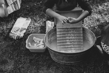 A child is washing clothes in an old zinc wash tub with wooden washboard  - 322083450
