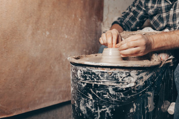 Man forms a white clay product on a pottery wheel