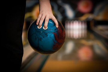 ten pin bowling ball being held in hand by bowler close up, with bowling lane and ten pins blurred...