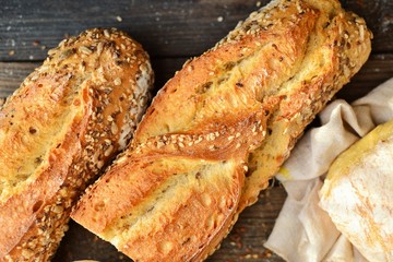 Baguette on a dark background, top view. Crispy bread with sunflower and flax seeds. Baguette cut in half.