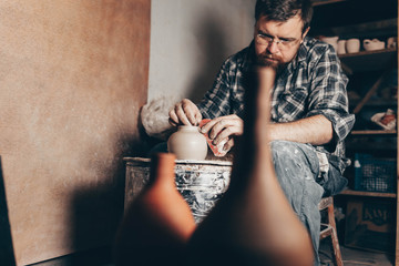 Pottery master works on pottery wheel in workshop