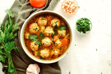 Soup with meatballs and vegetables on a white table background, top view. Vegetable soup with...