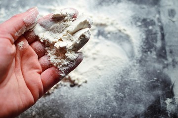 Flour in the hands of a woman. A woman pours flour on a black board. Ingredients, baking process.