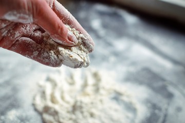 Fototapeta premium Flour in the hands of a woman. A woman pours flour on a black board. Ingredients, baking process.