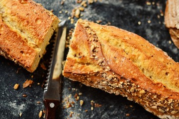 Baguette on a dark background, top view. Crispy bread with sunflower and flax seeds. Baguette cut in half.