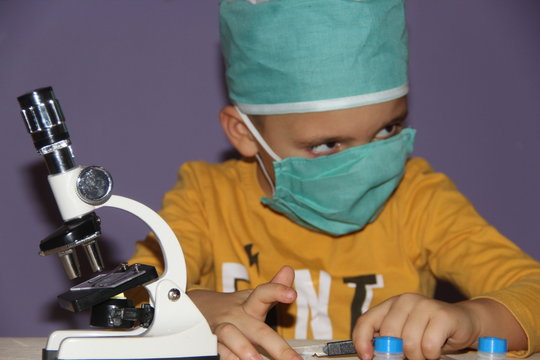 a boy in a medical mask near a microscope with a thoughtful look