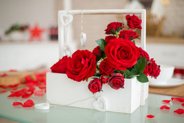 White basket with red roses on the table, rose petals, a romantic gift for Valentine's Day