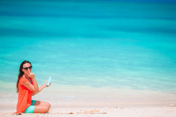 Beautiful young woman holding a suncream lying on tropical beach