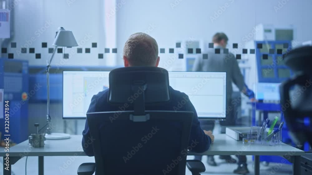 Poster Male Industrial Engineer Solving Problems, Working on a Personal Computer, Two Monitor Screens Show CAD Software with 3D Prototype of Zero-Emissions Engine Being Tested. Back View Zoom In