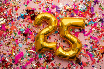 Number 25 gold birthday celebration balloon on a confetti glitter background