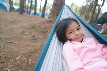 Asian child cute or kid girl sleeping relax on hammock and happy smiling on nature green tree and pine jungle or forest for holiday relaxation or camping tent picnic and travel trip on family vacation