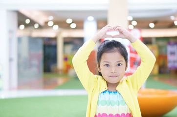 Asian child cute or kid girl lovely smiling and make heart by hand on head or Sarang-hae-yo for love valentine day or wedding with happy and enjoy with wear colorful dress yellow coat and cheerful