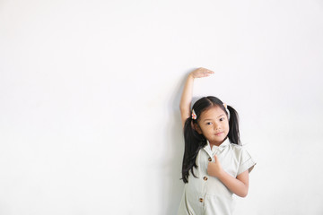 Obraz na płótnie Canvas asian child cute or kid girl happy smile show height or high and measure tall with growth by hand and arm up with show thumb finger for like and good on empty white wall background isolated with space