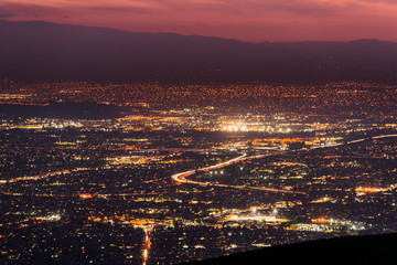 Panoramic night view of urban sprawl in San Jose, Silicon Valley, California; Visible light trail left by cars driving on one of the freeways; long exposure